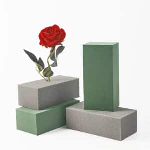 Sur un fond blanc 2 briques de mousse vertes et 2 grises superposées avec une rose avec feuillage plantée dedans.