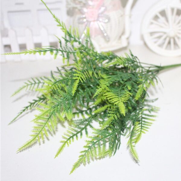 Une branche de fougère artificielle verte poser sur une table blanche.