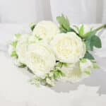 Bouquet de pivoines blanches posé sur une table blanche derrière un rideau blanc