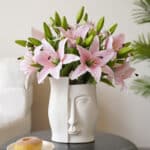 Bouquet de lys artificiel rose dans un vase avec un visage.
