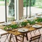 Table en bois avec le couvert, des bougies dorées et une guirlande de feuilles de lierre sur le chemin de table.