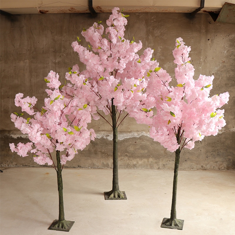 3 cerisiers artificiels en fleurs roses de tailles différentes dans une pièce au sol beige.