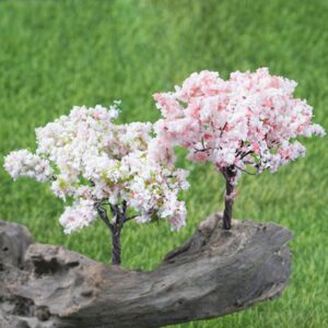 Deux cerisiers artificiels en fleurs blanc et rose sur un tronc en bois au milieu de l'herbe.