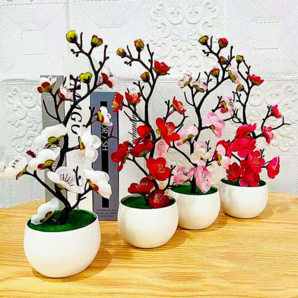 Des branches de cerisiers en fleurs de couleurs différentes dans des pots blancs rond sur une table en bois clair devant un mur blanc.