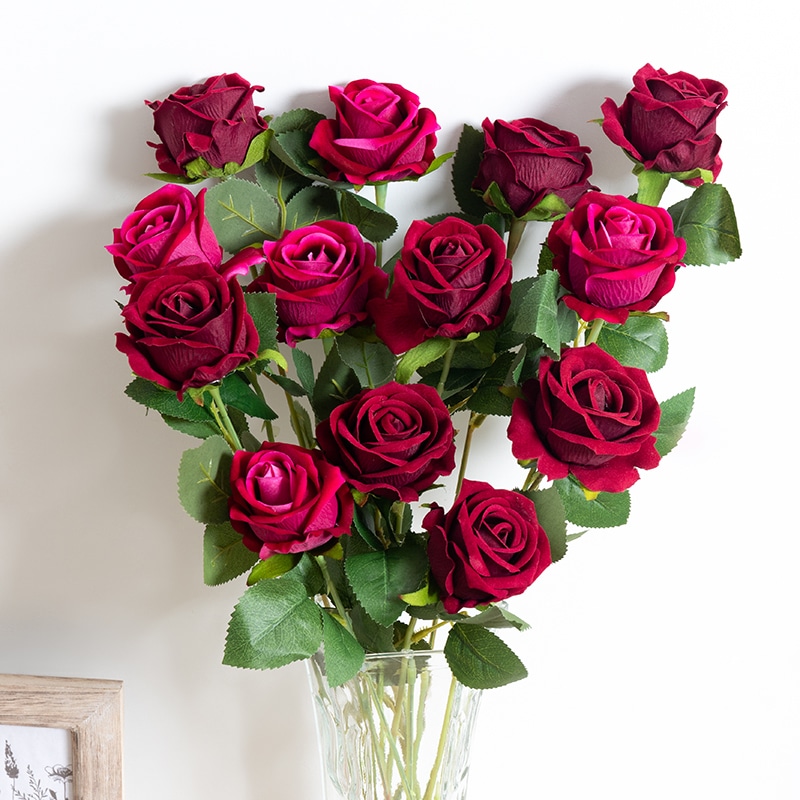 Un bouquet de roses rouges dans un vase transparent face à un mur blanc.