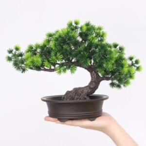 Plante artificiel Bonsaï de pin en plastique mise en pot tenue par une main.