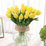 Bouquet de tulipes jaunes dans une vase transparent posé sur une table avec une nappe blanche