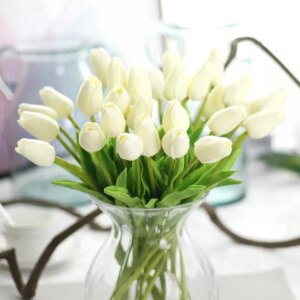 Bouquet de tulipes blanches dans un vase transparent posé sur une table.