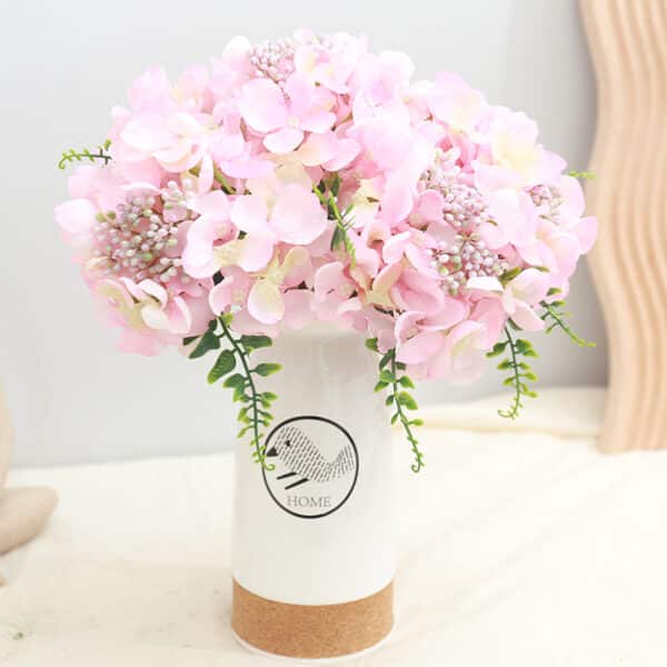 Bouquet d'hortensias rose dans un vase blanc posé sur un meuble blanc.