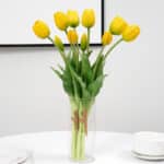 Bouquet de tulipes jaune dans un vase transparent sur une table blanche sur un fond gris.