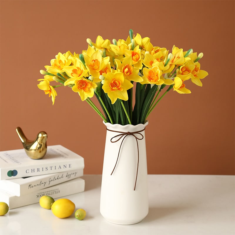 Bouquet de narcisse jaune dans un vase en terre blanc sur une table blanche avec des livre et des citrons.