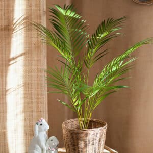 Feuilles de palmier vertes en plastique dans un pot en osier posé sur une table.