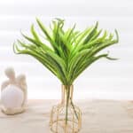 Feuilles et tige artificielles de plante de palmier dans un vase or transparent.