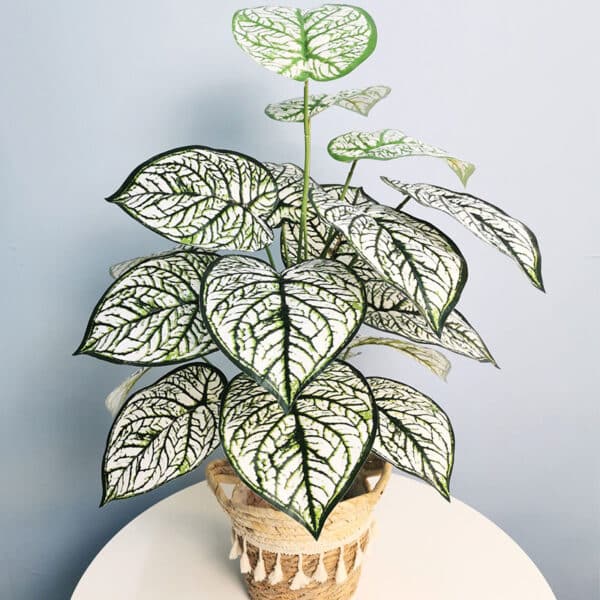Plante artificielle à feuilles vertes blanches dans un pot posé sur une table.