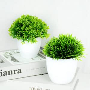 Deux petit pots de plantes artificielles verte une sur un table l'autre sur un livre