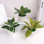 Trois petites plantes vertes artificielles dans des pots blancs posés sur un meuble blanc.
