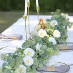Guirlande artificielle d'eucalyptus et de roses blanches pour intérieur et extérieur posée sur une table en décoration.