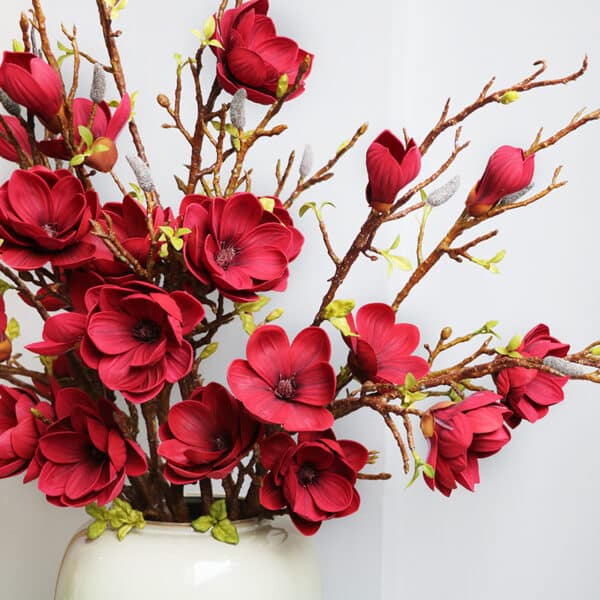 Bouquet de magnolias rouges avec des branches dans un vase blanc.
