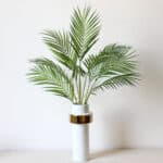 Photo de branches de palmier artificielles dans un vase blanc.
