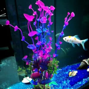 Plante d'aquarium artificielle violette dans l'eau avec un poisson au second plan.