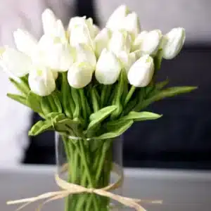 Bouquet de tulipes beige en plastique dans un vase transparent sur une table grise