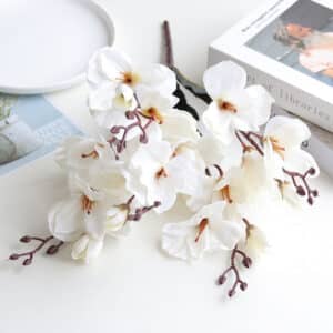 Petit bouquet de magnolias en plastique de couleur blanche sur une table banche avec une assiette et un livre