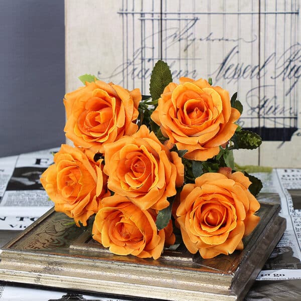 Bouquet de six roses oranges posé sur un livre posé sur une table derrière un fond gris.