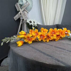 Tige de dauphinelles orange sur une table grise sur un fond gris avec un rideau blanc.